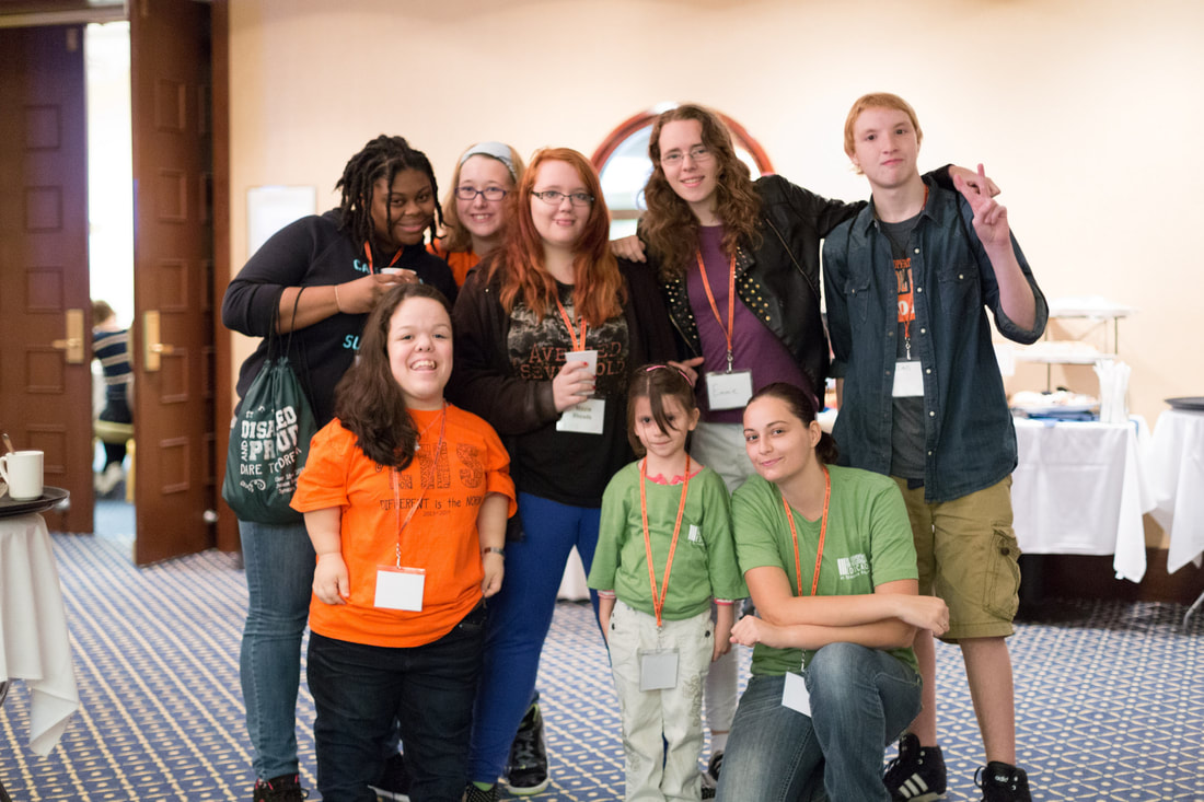 Picture of group of students, some wearing green Disabled & Proud conference t-shirts.  Group is diverse including students of color, a mom with her dauther, and a little person