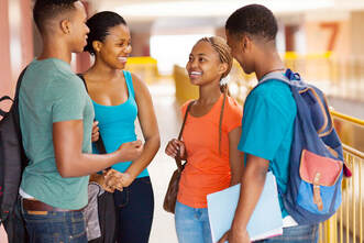 Picture of four Black high school students talking in a school hallway.  Two appear male and two appear female.  Two are wearing a backpack and one has a purse.
